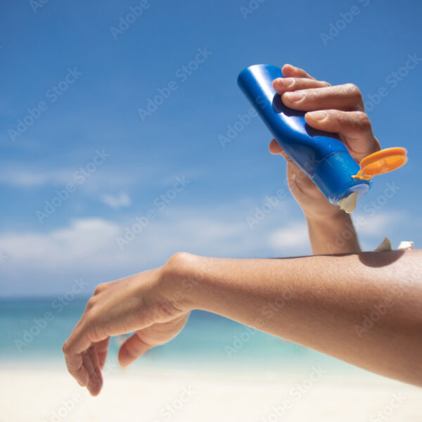 Woman applying sunscreen on her hands from a bottle on the beach with the sea in the background. SPF sunblock protection concept.selective focus